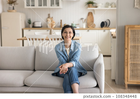 Happy middle-aged housewife relaxing sit on sofa at home Happy middle-aged housewife relaxing sit on sofa at home 108348448