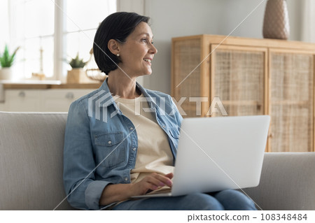 Older woman put laptop on laps sitting on couch Older woman put laptop on laps sitting on couch 108348484