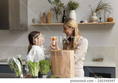 Happy mother and baby daughter kid producing vegetables from bag Happy mother and baby daughter kid producing vegetables from bag 108348947