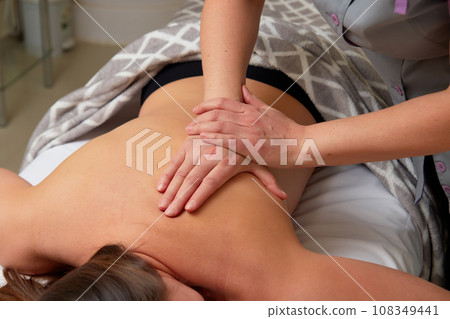 Massagist performing back massage to female client. Massagist performing back massage to female client. 108349441