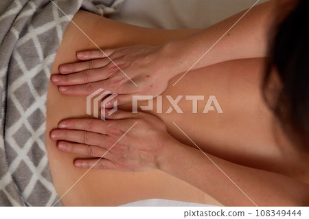 Massagist performing back massage to female client. 108349444