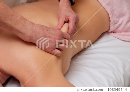 Massagist performing back massage to female client. Massagist performing back massage to female client. 108349544