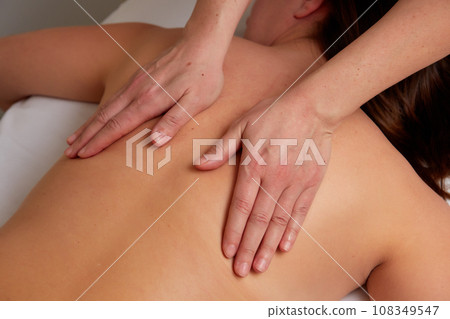 Massagist performing back massage to female client. Massagist performing back massage to female client. 108349547