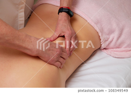 Massagist performing back massage to female client. 108349549
