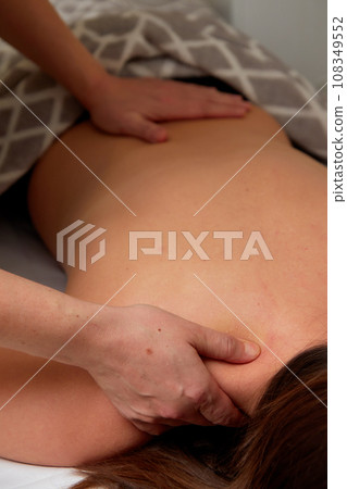Massagist performing back massage to female client. Massagist performing back massage to female client. 108349552