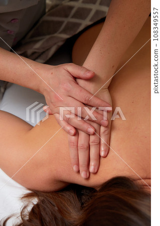 Massagist performing back massage to female client. Massagist performing back massage to female client. 108349557