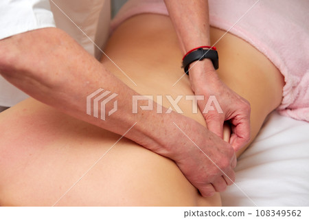 Massagist performing back massage to female client. Massagist performing back massage to female client. 108349562