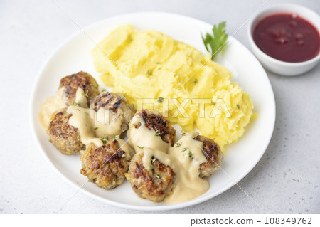 Swedish noisettes (fricandel) with mashed potatoes, Brune Sos creamy sauce and lingonberry (cranberry) sauce. Traditional meatballs with garnish. Selective focus, close-up. Swedish noisettes (fricandel) with mashed potatoes, Brune Sos creamy sauce and lingonberry (cranberry) sauce. Traditional meatballs with garnish. Selective focus, close-up. 108349762
