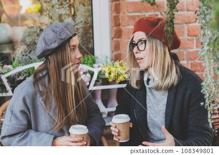 Young female best friends talking to each other discussing interesting themes during free time hipster girls joking and having fun together enjoying recreation with coffee to go on urban background 108349801