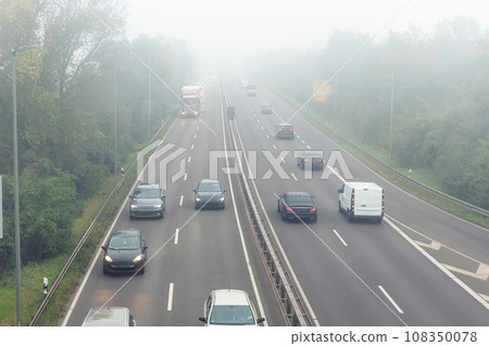 Scenic city highway road traffic jam many cars at foggy misty rainy haze morning low poor visibility cold spring autumn season. Seasonal bad rainy weather accident danger warning car fog light 108350078