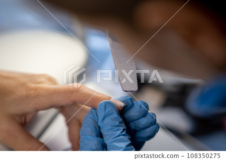 Nail care procedure in a beauty salon. Female hands and tools for manicure, process of performing manicure in beauty salon. Concept spa body care. Gloved hands of a skilled manicurist cutting cuticles Nail care procedure in a beauty salon. Female hands and tools for manicure, process of performing manicure in beauty salon. Concept spa body care. Gloved hands of a skilled manicurist cutting cuticles 108350275