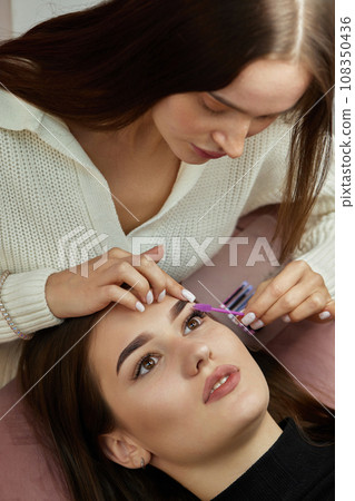 master combs the eyelashes of the client after the eyelash extension procedure. Cosmetology and skin care 108350436