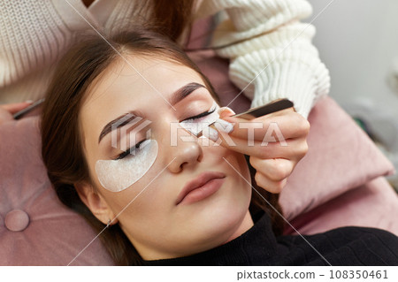 cosmetologist removes glue cotton tape under eye. Eyelash extension procedure cosmetologist removes glue cotton tape under eye. Eyelash extension procedure 108350461