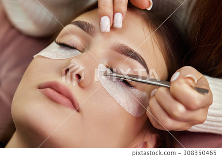 Hands of master preparing glue cotton tape under eye before eyelash extension procedure 108350465