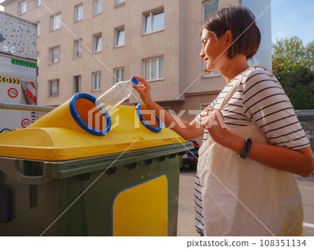 woman throwing plastic bottle Recycling bin stand on european street. Waste separation rubbish before drop to garbage bin to save world, environment care. Pollution trash recycling management concept woman throwing plastic bottle Recycling bin stand on european street. Waste separation rubbish before drop to garbage bin to save world, environment care. Pollution trash recycling management concept 108351134
