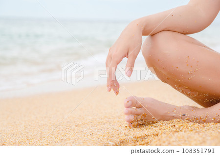 woman sits on the shore and relaxes. A woman's leg and hand on her knee, a girl sitting on the sea sand on the beach on a summer day, close-up 108351791