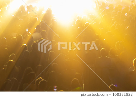 A concert crowd illuminated by bright yellow lights. 108351822