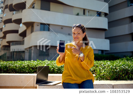 Smiling happy woman pointing her finger aside a copy ad space on her smartphone with black blank mockup digital screen Smiling happy woman pointing her finger aside a copy ad space on her smartphone with black blank mockup digital screen 108353529