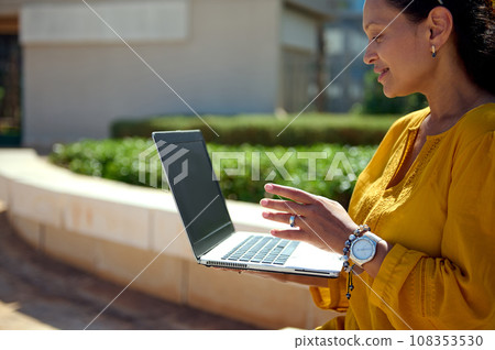 Close-up multi ethnic woman talking with business partners via video link, using a laptop with black blank mockup screen Close-up multi ethnic woman talking with business partners via video link, using a laptop with black blank mockup screen 108353530