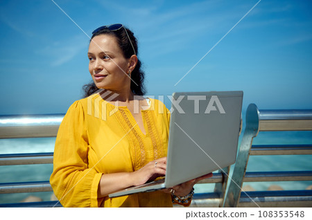 Smiling businesswoman, entrepreneur freelancer looking aside, standing with laptop against the ocean background Smiling businesswoman, entrepreneur freelancer looking aside, standing with laptop against the ocean background 108353548