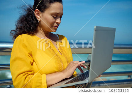 Close-up portrait of a middle aged business woman using laptop, typing text, working online against seashore background 108353555