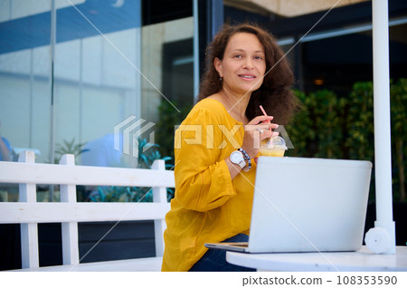 Happy successful middle aged woman, entrepreneur drinking freshly squeezed juice and working online on laptop in a cafe 108353590