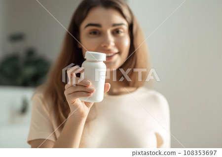 Food supplement. Young woman holding a white jar bottle of vitamins or pills. Place for your logo 108353697