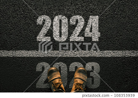 Man walks on asphalt and crosses the line by 2024. New year 2024. Men's legs with leather shoes go to 2024. End of 2023 and beginning of 2024 108353939