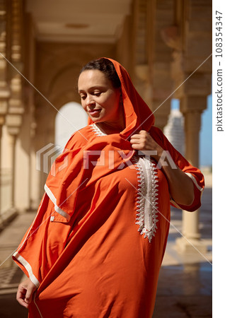 Beautiful Middle Eastern woman, in ethnic Oriental attire, looking down, standing against a marble arch background Beautiful Middle Eastern woman, in ethnic Oriental attire, looking down, standing against a marble arch background 108354347
