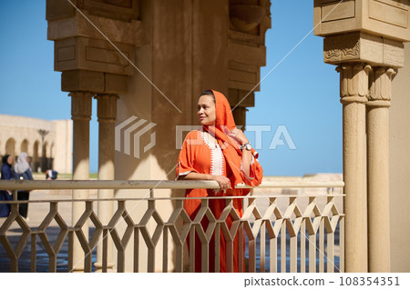 Gorgeous Middle Eastern Muslim woman with head covered in hijab and ethnic dress, smiles looking aside, Hassan II mosque Gorgeous Middle Eastern Muslim woman with head covered in hijab and ethnic dress, smiles looking aside, Hassan II mosque 108354351
