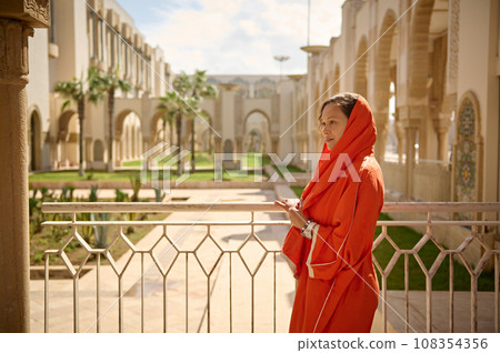 Beautiful Middle Eastern Muslim woman with head covered in hijab, standing with cupped hands at Hassan II mosque Beautiful Middle Eastern Muslim woman with head covered in hijab, standing with cupped hands at Hassan II mosque 108354356