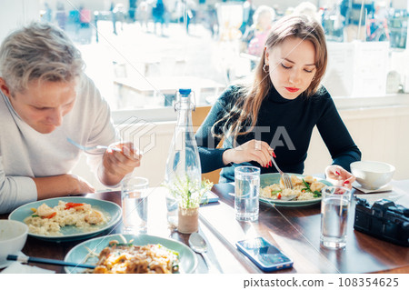 Young female and male friends sitting at served table in casual cafe and eating delicious hot risotto with shrimps or curry rice during lunch break. Trying new foods while traveling. real people. 108354625