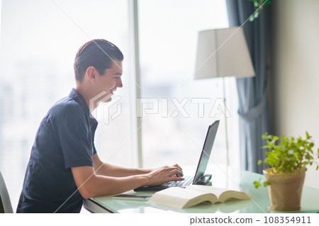 Woman working at laptop at big window with city view Woman working at laptop at big window with city view 108354911