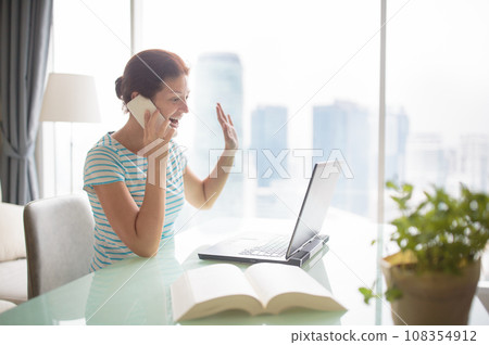 Woman working at laptop at big window with city view Woman working at laptop at big window with city view 108354912