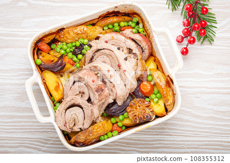 Festive Christmas rolled sliced pork roasted in white casserole dish with potatoes, vegetables and herbs on rustic white wooden background top view. Baked pork roll with vegetables for Xmas dinner Festive Christmas rolled sliced pork roasted in white casserole dish with potatoes, vegetables and herbs on rustic white wooden background top view. Baked pork roll with vegetables for Xmas dinner 108355312