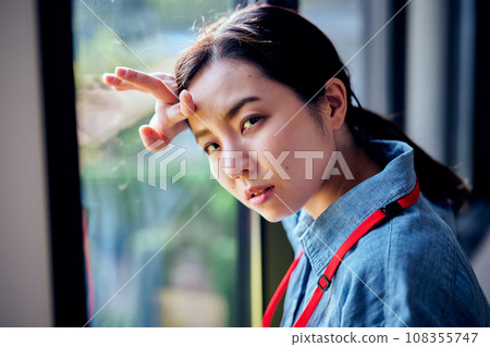 Young woman putting her hand on her head by the window Young woman putting her hand on her head by the window 108355747