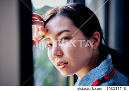 Young woman putting her hand on her head by the window Young woman putting her hand on her head by the window 108355748