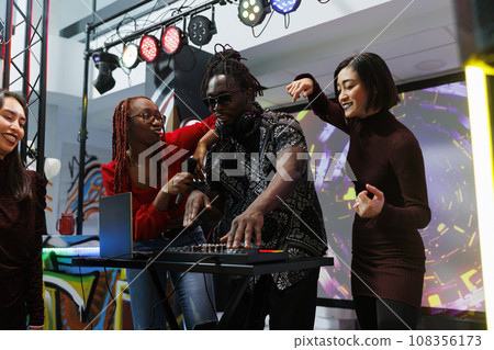 Band using dj station and dancing on stage at disco gathering in nightclub. African american frontman playing whille diverse women moving and engaging crowd to party at live concert Band using dj station and dancing on stage at disco gathering in nightclub. African american frontman playing whille diverse women moving and engaging crowd to party at live concert 108356173
