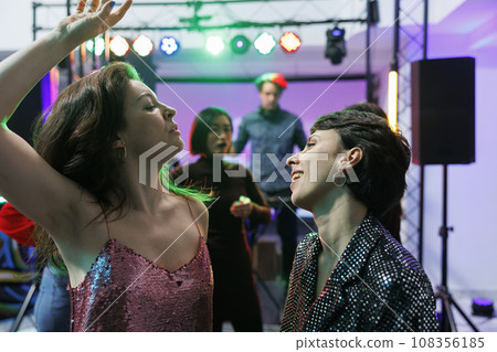 Carefree girlfriends dancing and celebrating together at nightclub party event. Young women making energetic moves on dancefloor while relaxing at social gathering in club Carefree girlfriends dancing and celebrating together at nightclub party event. Young women making energetic moves on dancefloor while relaxing at social gathering in club 108356185