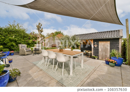 a patio area with chairs, tables and an umbrella over the dining table in front of a wooden shed behind a patio area with chairs, tables and an umbrella over the dining table in front of a wooden shed behind 108357630