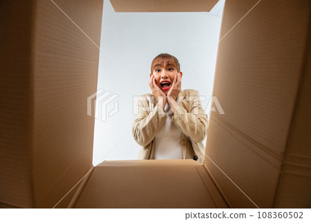 A young woman opens up a box, surprised and happy to see their order better than expected A young woman opens up a box, surprised and happy to see their order better than expected 108360502