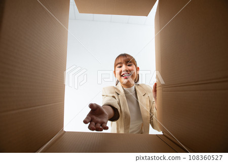 Smiling young woman opening a carton box, relocation and unpacking concept Smiling young woman opening a carton box, relocation and unpacking concept 108360527