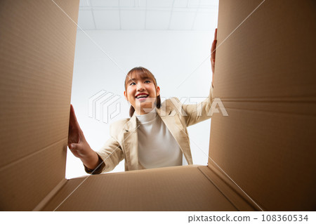smiling female surprised unpacking christmas gift big box and looking inside, inside bottom view 108360534