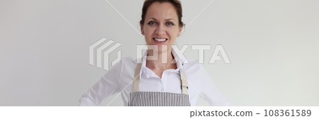Young woman puts on striped apron smiling with satisfaction 108361589