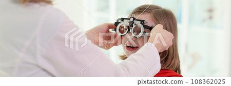 Doctor puts ophthalmology goggles on girl to check eyesight Doctor puts ophthalmology goggles on girl to check eyesight 108362025
