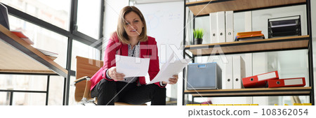 Focused woman in pink jacket sits on chair reading papers Focused woman in pink jacket sits on chair reading papers 108362054