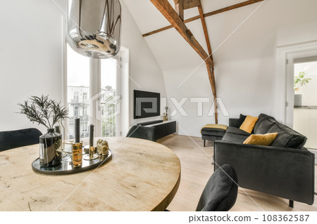 a living room with wood flooring and white walls, including a round wooden table surrounded by black leather chairs 108362587