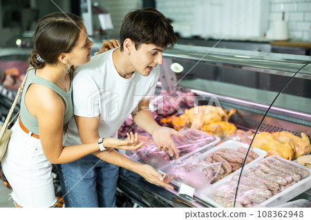 Young man and woman purchasers buying sausages in butcher shop 108362948