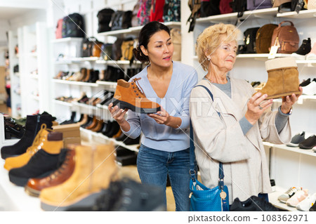 Consultant in shoeshop helping old woman to choose footwear Consultant in shoeshop helping old woman to choose footwear 108362971