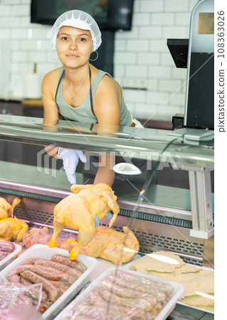 Positive young saleswoman demonstrating chicken in butcher shop Positive young saleswoman demonstrating chicken in butcher shop 108363026